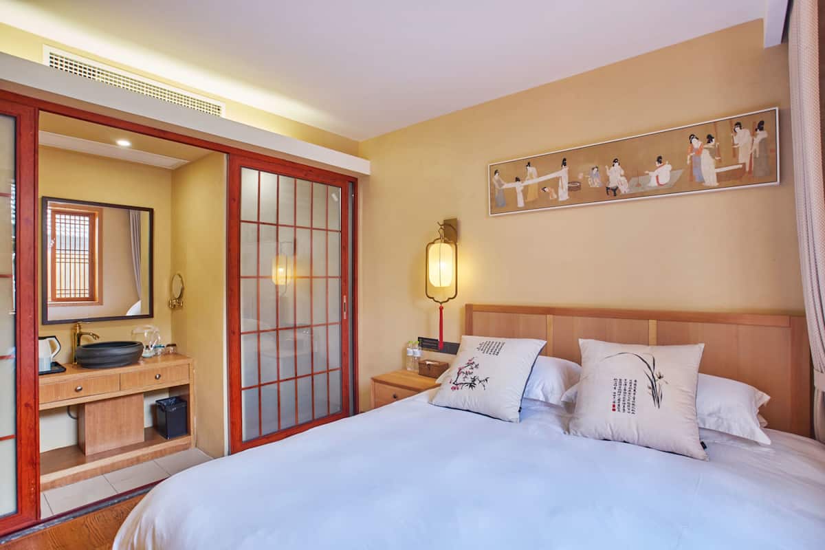 Een hotelkamer met een bed, een nachtkastje van hout, een spiegel, een wastafel en een schuifdeur.