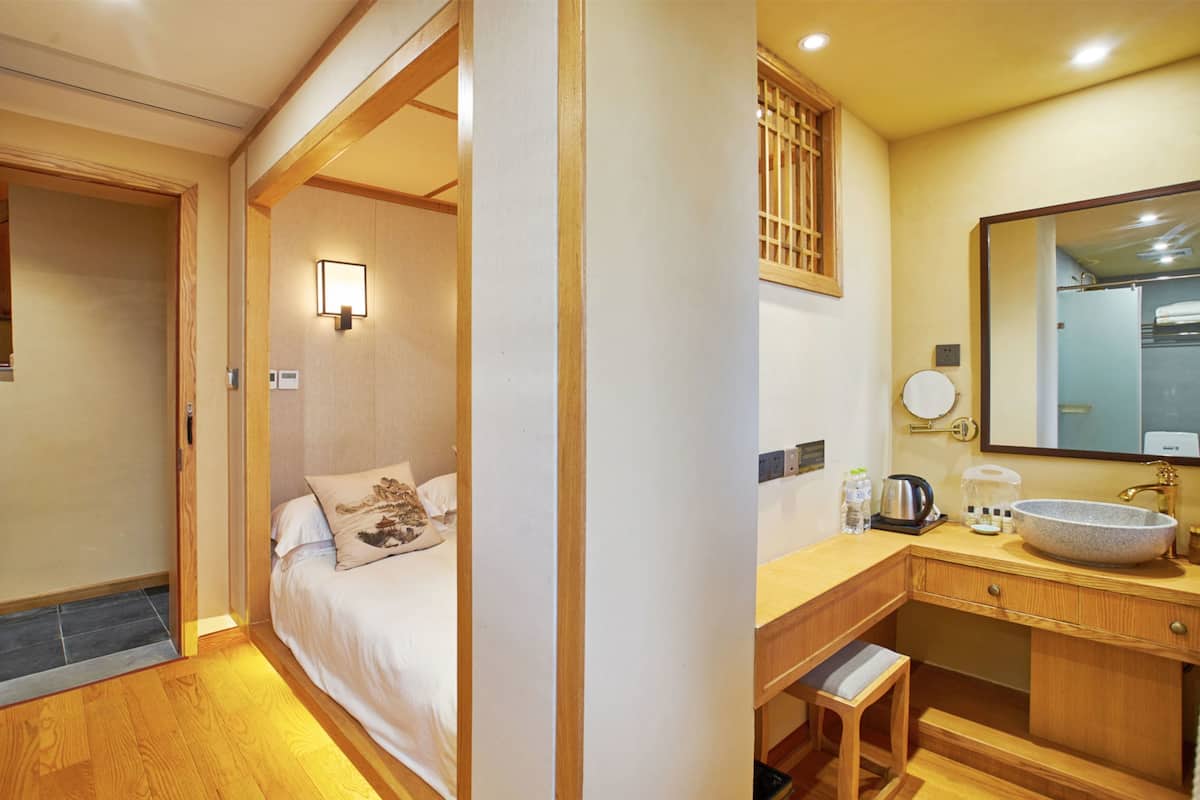 Een hotelkamer met een bed, nachtkastje en een badkamer met een wastafel en spiegel.