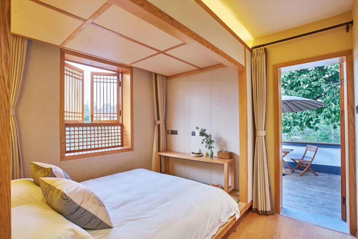 Een traditionele Japanse slaapkamer met tatami vloeren, een laag houten bed, een schuiframen schot en een balkon met uitzicht op groen.