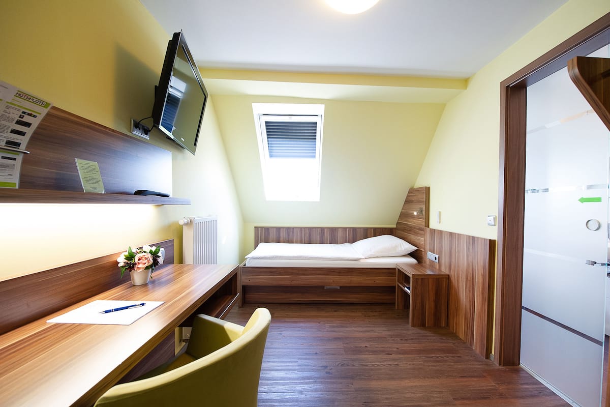 A compact room with a wooden desk, a bed, a television, and a small window.