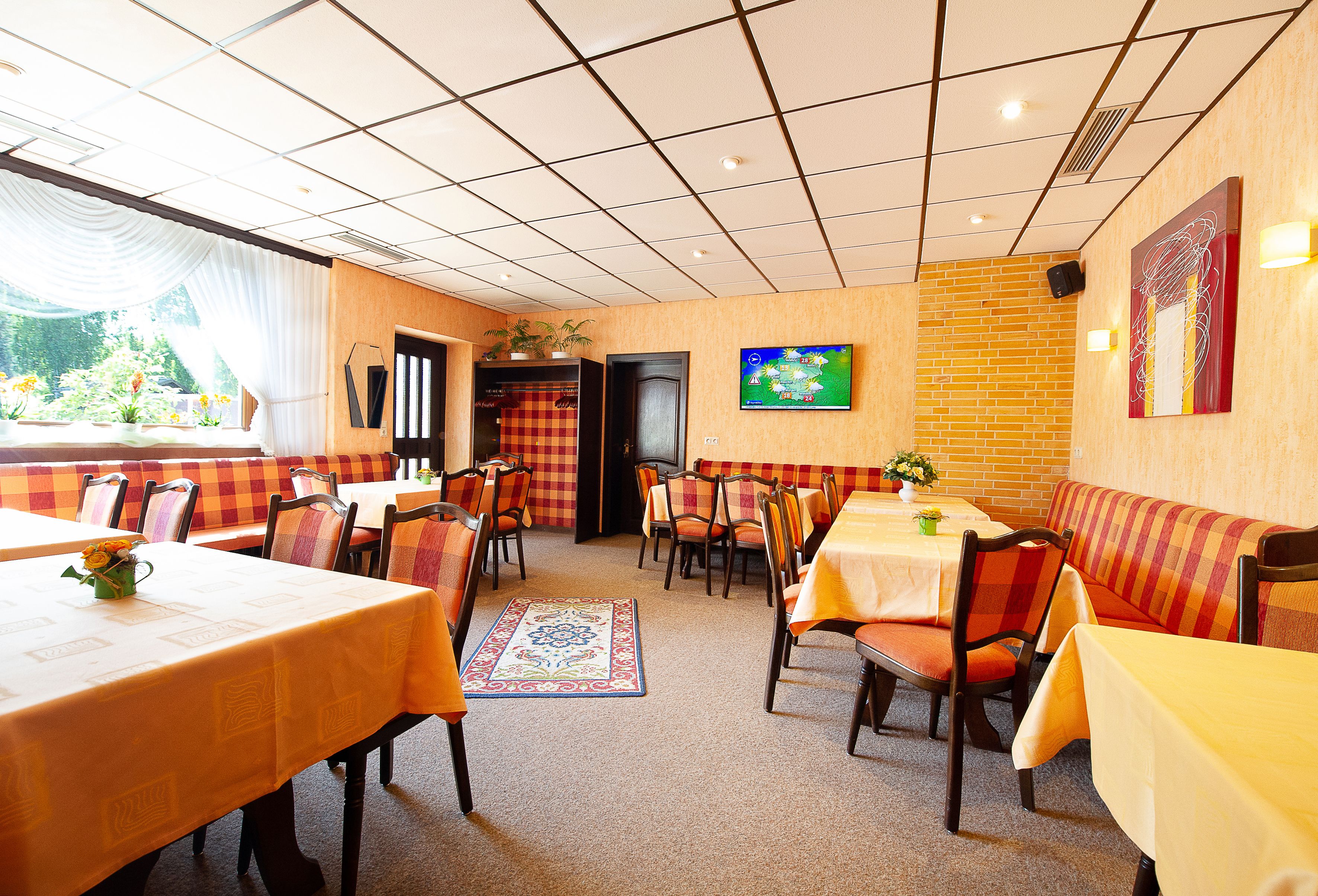 A restaurant with booths and tables, a TV on the wall, and a view of the outdoors.