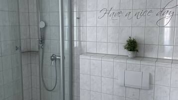Une salle de bain moderne avec une douche en verre, des toilettes blanches et une petite plante en pot accrochée au mur.