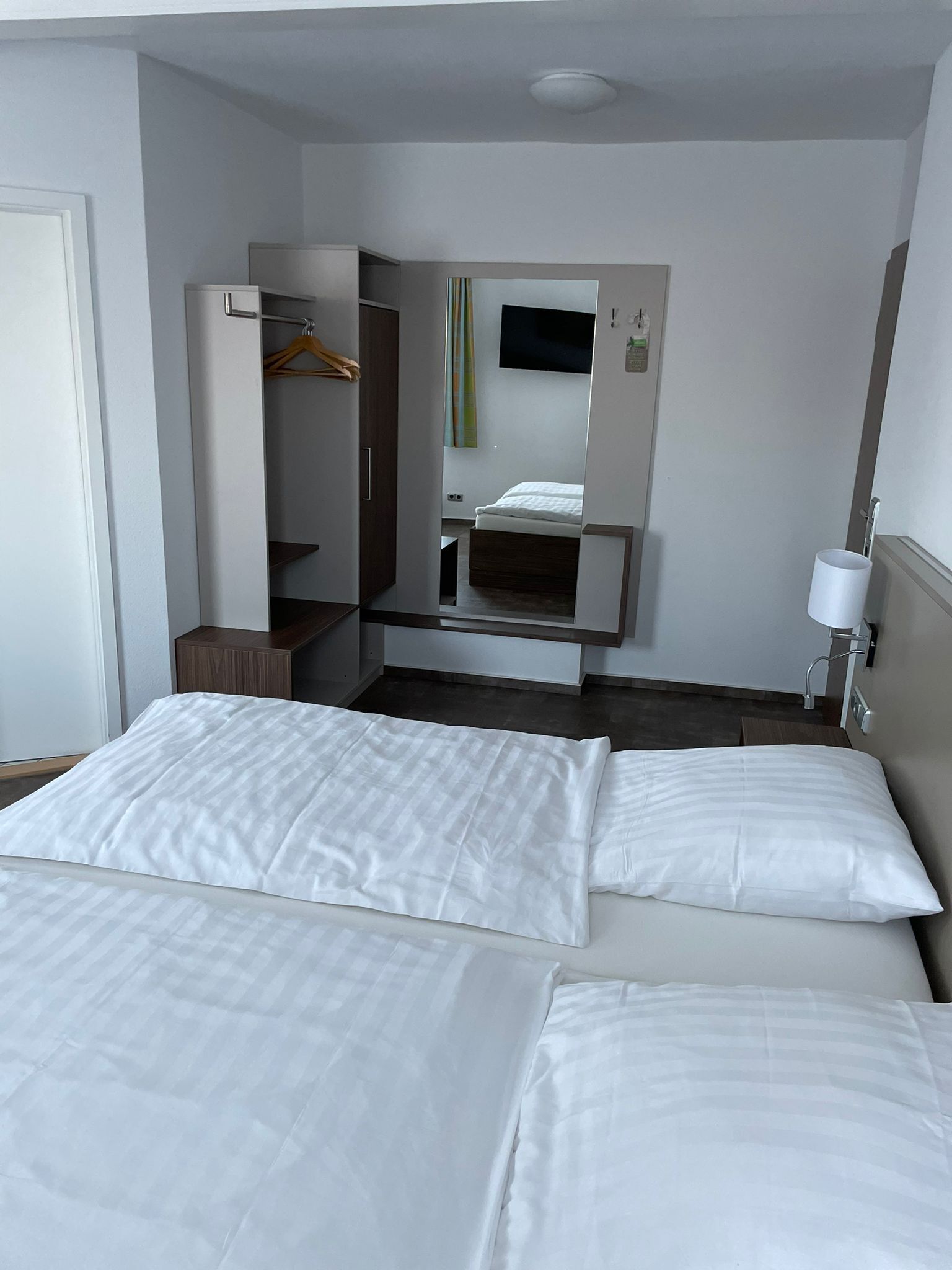Una habitación de hotel con dos camas, un armario, un televisor y una lámpara de noche.