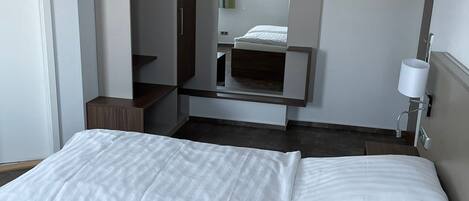 Una habitación de hotel con dos camas, un armario, un televisor y una lámpara de noche.