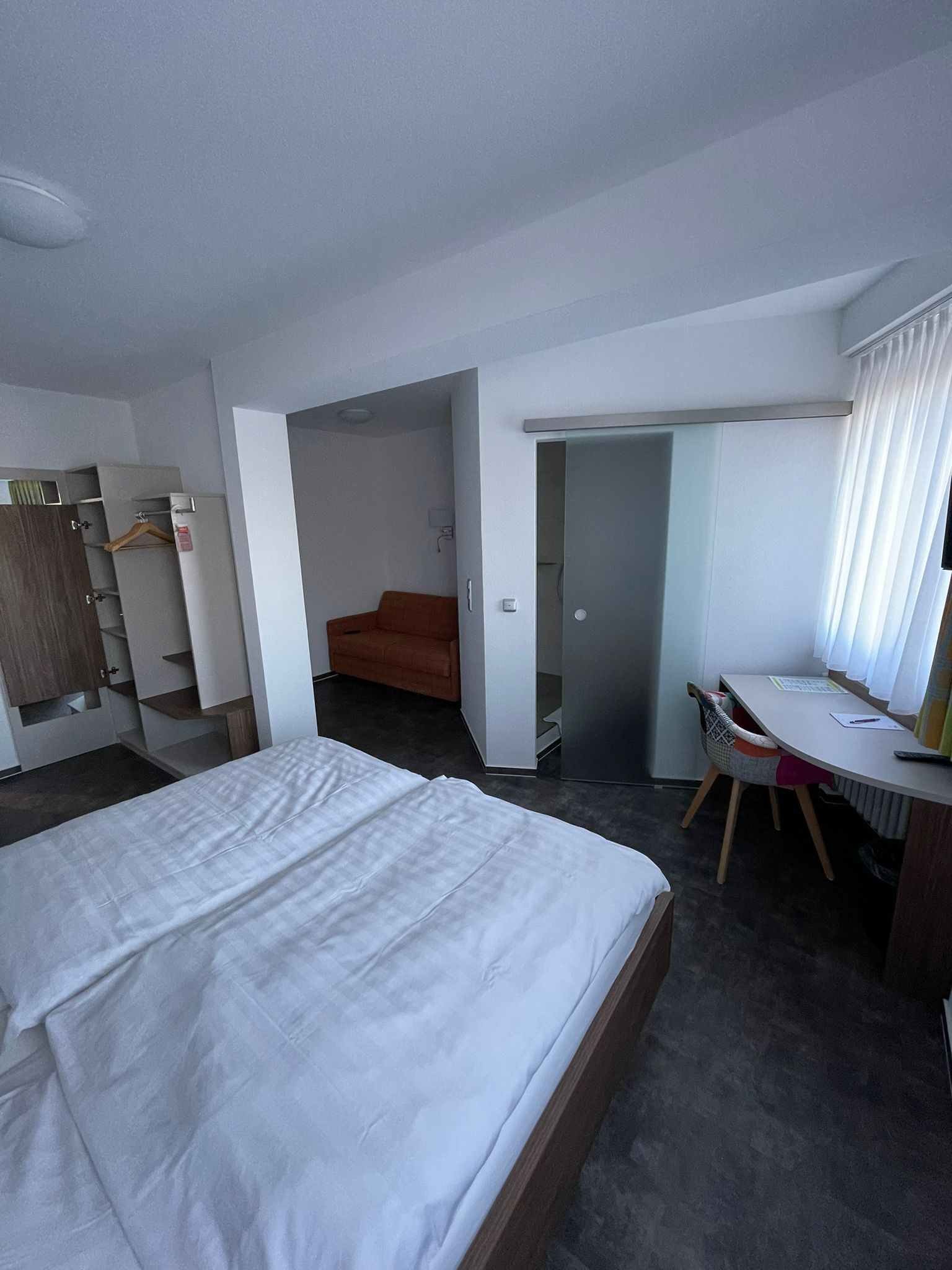 Habitació d'hotel amb llit, escriptori, cadira, armari i bany.