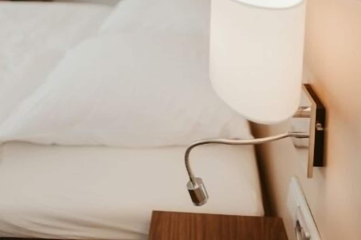 A hotel room with a bed, a bedside lamp, and a wall-mounted light fixture.