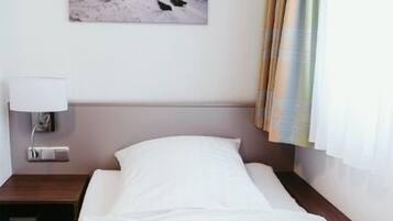 A hotel room with a bed, a nightstand, a lamp, a painting of a snowy landscape, and a curtain.