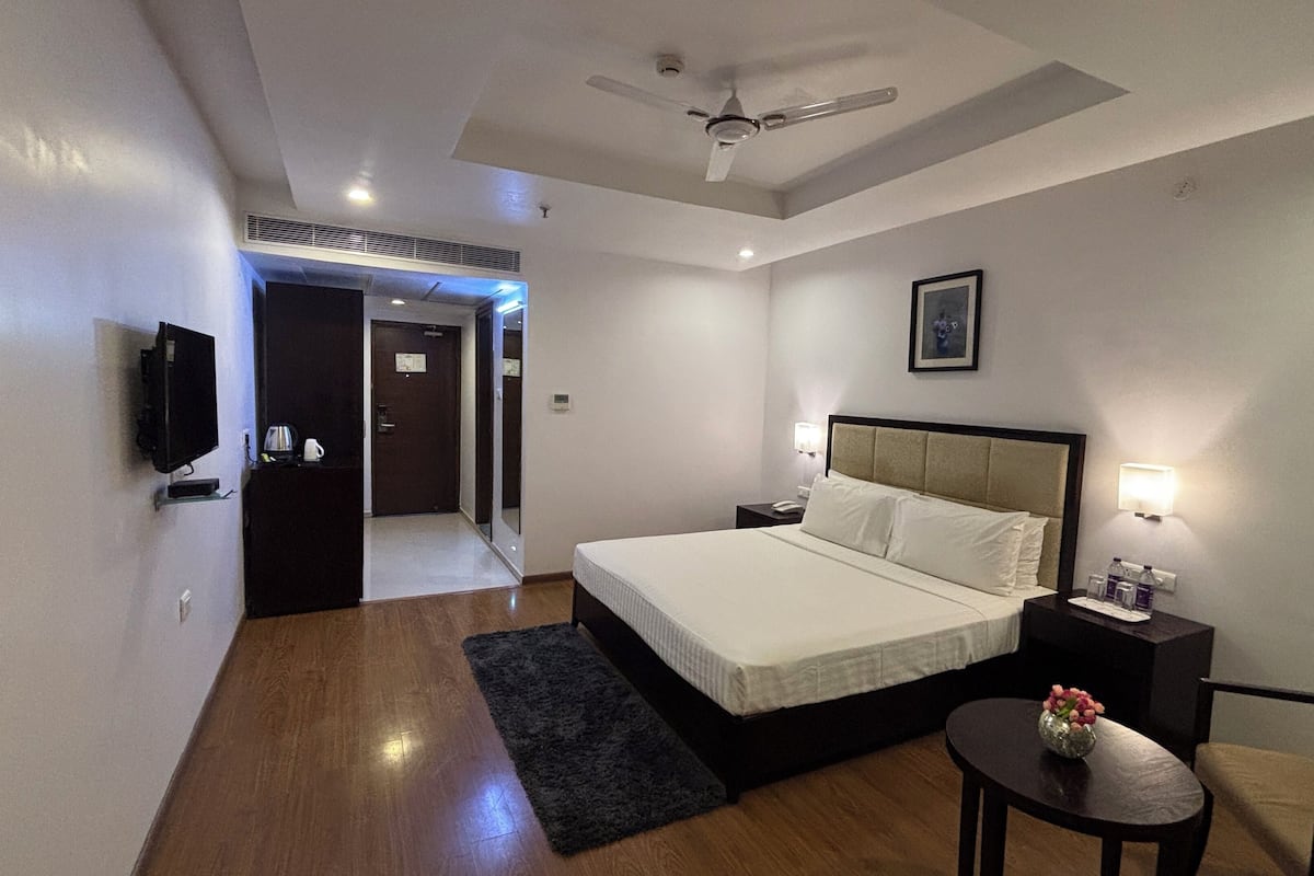 A hotel room with a bed, bedside tables, a chair, a desk, a ceiling fan, and a door leading to a hallway.