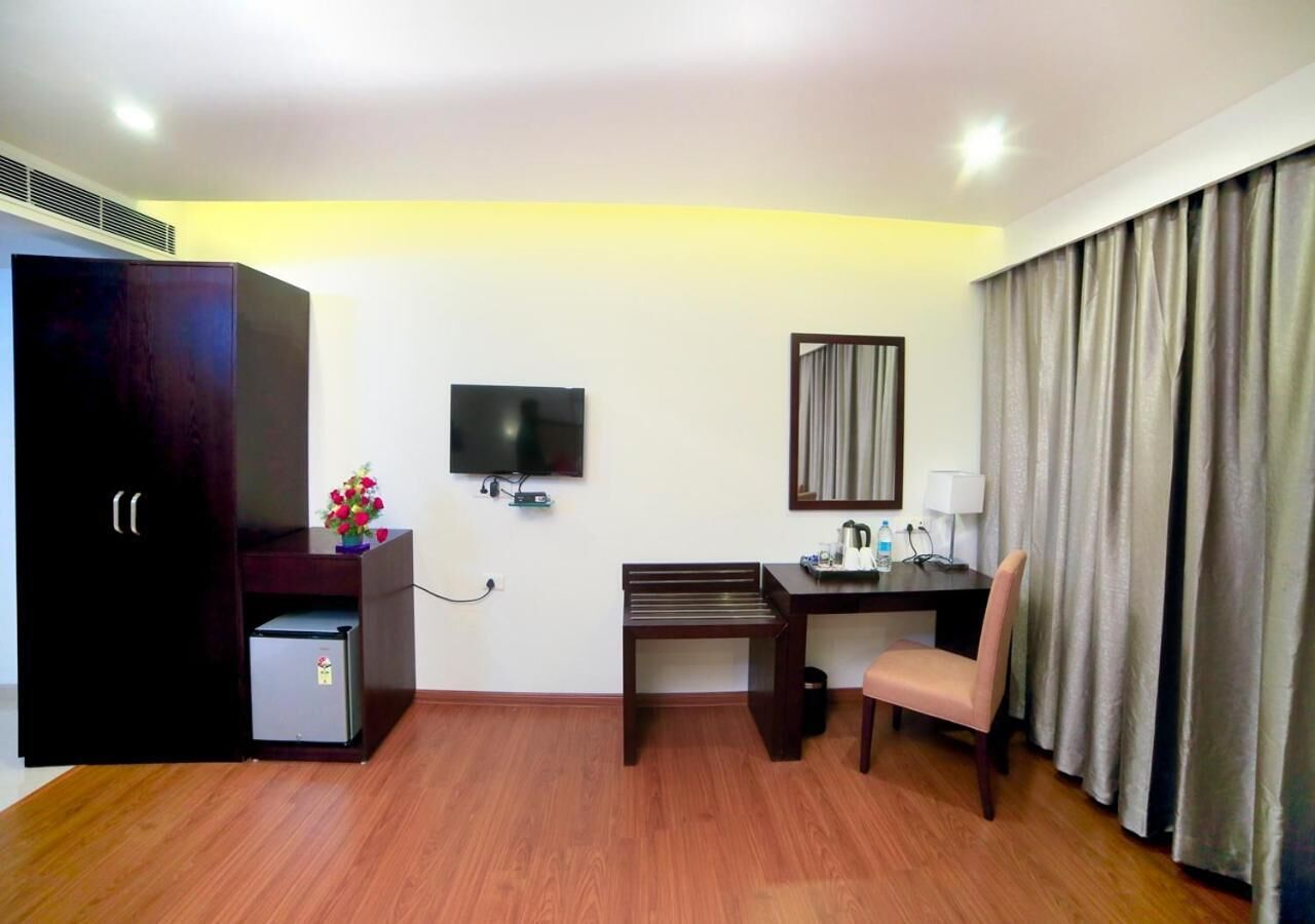 Ein Hotelzimmer mit Holzboden, Schreibtisch mit Stuhl, Fernseher, Kleiderschrank und kleinem Kühlschrank.