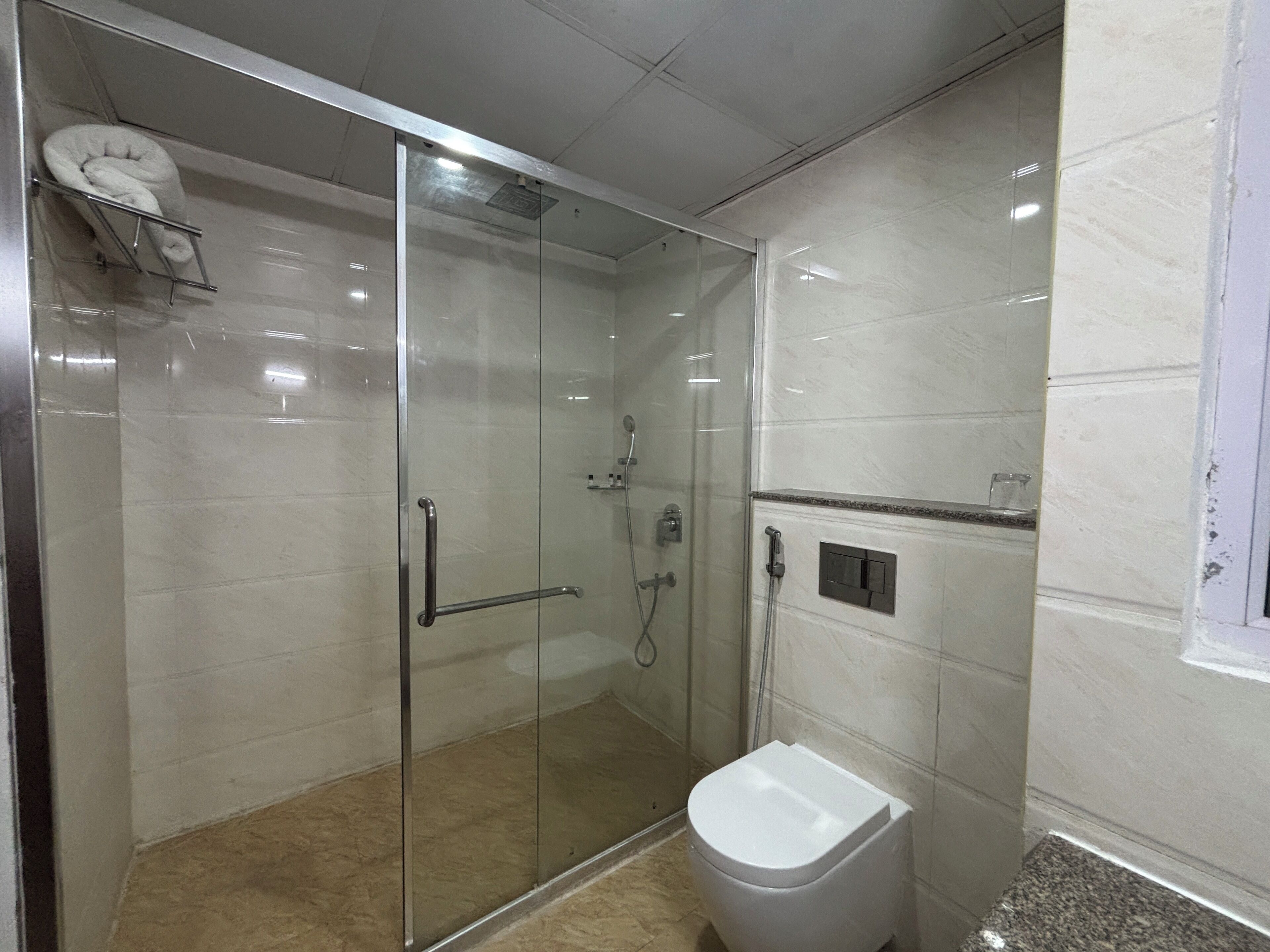 A modern bathroom with a glass-enclosed shower, a white toilet, and a marble-tiled floor.