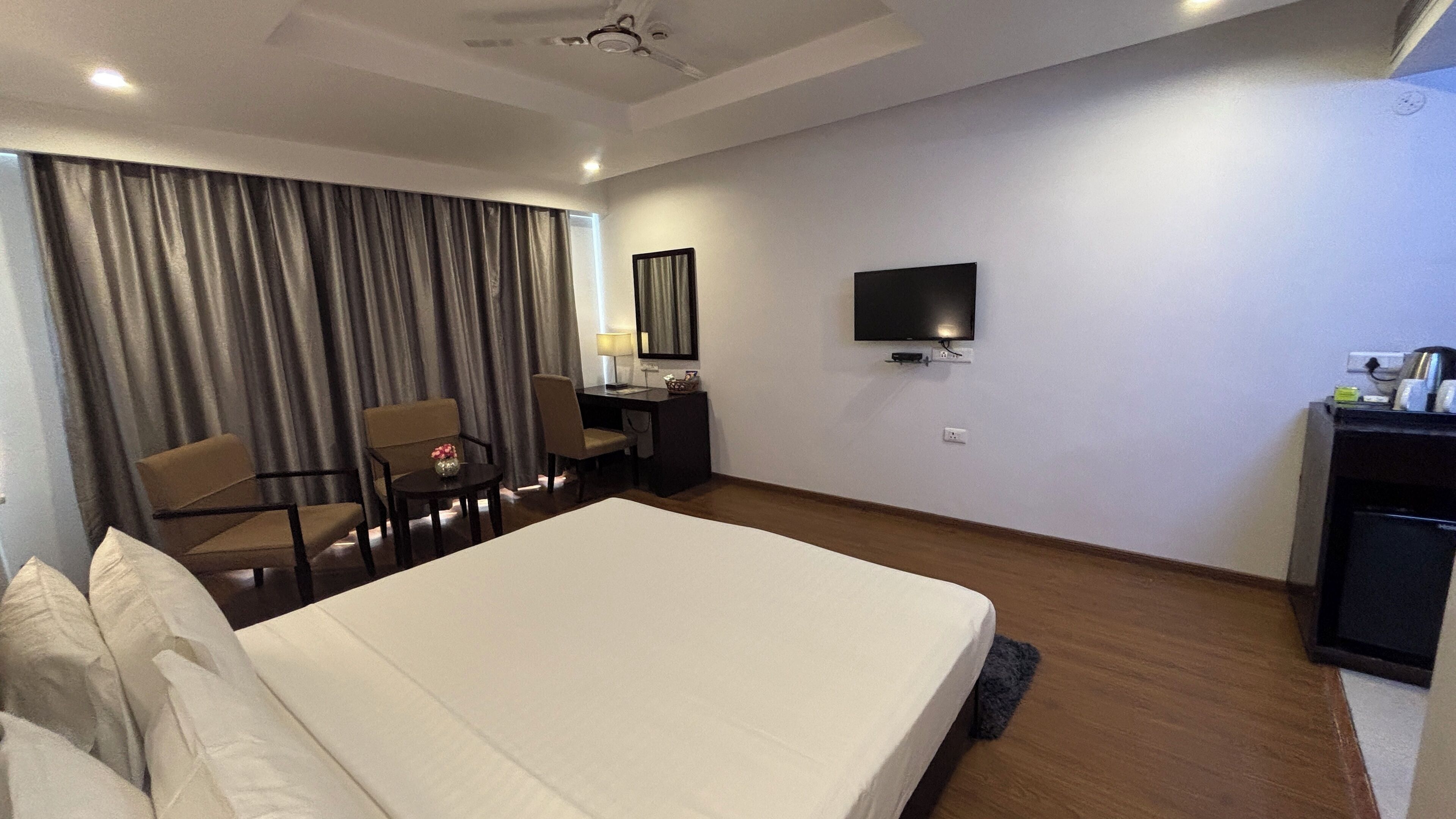 A hotel room with a large bed, a desk with a chair, a television, and a wardrobe.