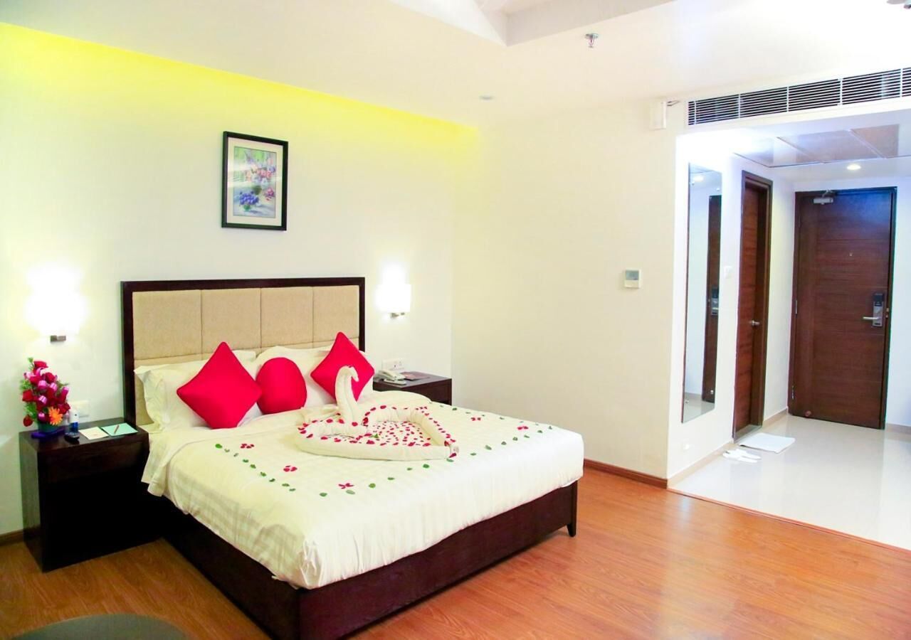 Una cama bien hecha con almohadas rojas, una mesita de noche con un florero y un cuadro en la pared.