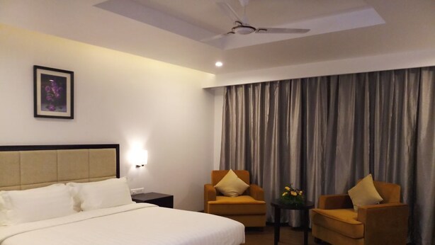 A hotel room with a large bed, two armchairs, a small table with a vase, and a ceiling fan.