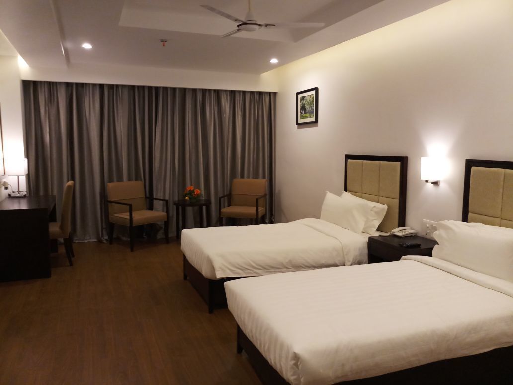 A hotel room with two beds, a desk, a chair, and a window with curtains.