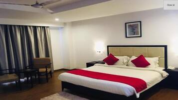 A hotel room with a bed, a desk, a chair, a nightstand, and a window with curtains.