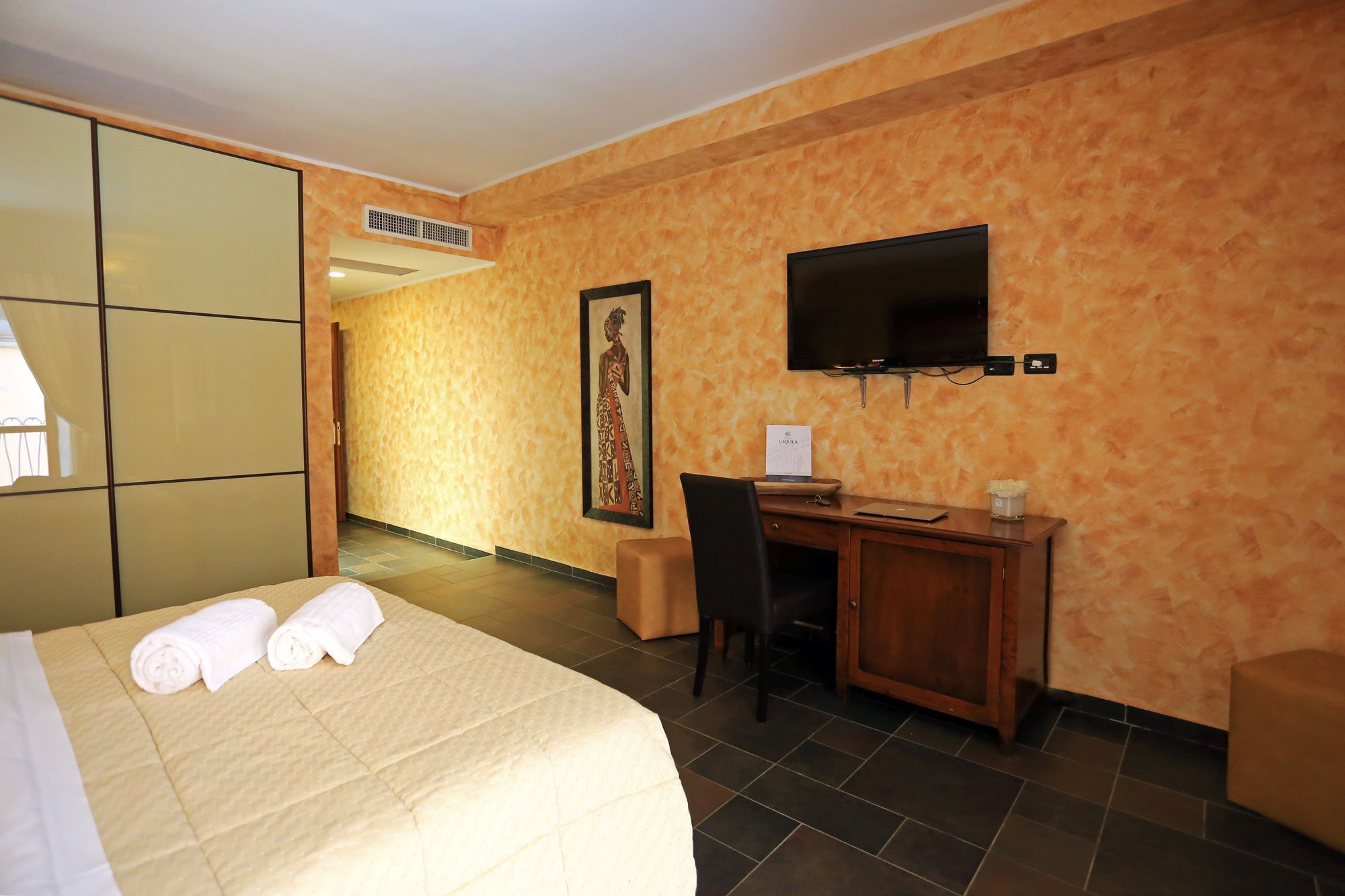 A hotel room with a bed, a desk, a chair, a television, and a painting on the wall.