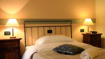 A neatly made bed with a white duvet and a blue floral pillow, flanked by two bedside tables with lamps, one of which has a telephone.