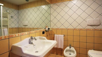 A bathroom with a sink, bidet, and toilet, tiled in a diamond pattern with a beige and white color scheme.