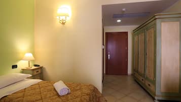 Habitación de hotel con cama, mesita de noche con lámpara, armario y puerta que da a otra habitación.