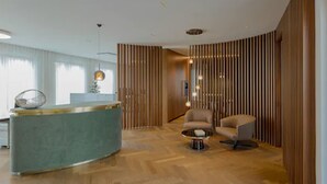 A modern reception area with a curved reception desk, a round coffee table, and a seating area with a chair. - DD Suites Serviced Apartments (Munich)