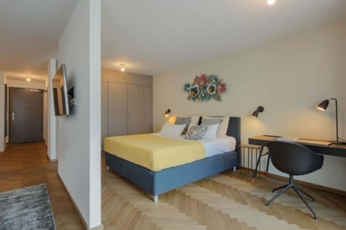 A bedroom with a bed, desk, chair, and artwork on the wall.