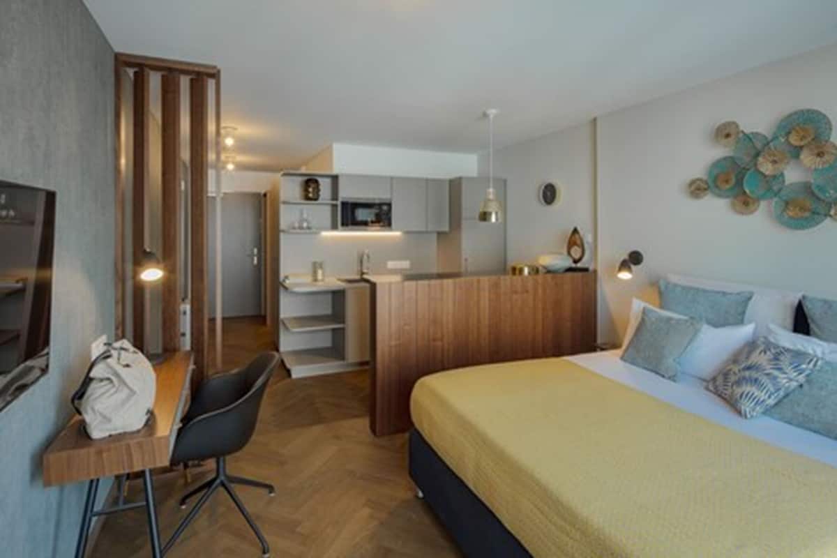 A compact hotel room with a bed, a desk, and a kitchenette.