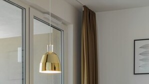 A modern room with a glass door, a round table with a white base, a black chair, and a pendant light. - DD Suites Serviced Apartments (Munich)