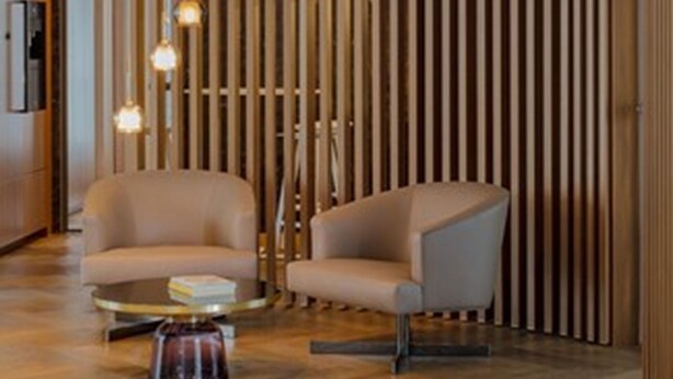 A modern lobby with two armchairs, a round coffee table, and a vertical wooden panel wall. - DD Suites Serviced Apartments (Munich)