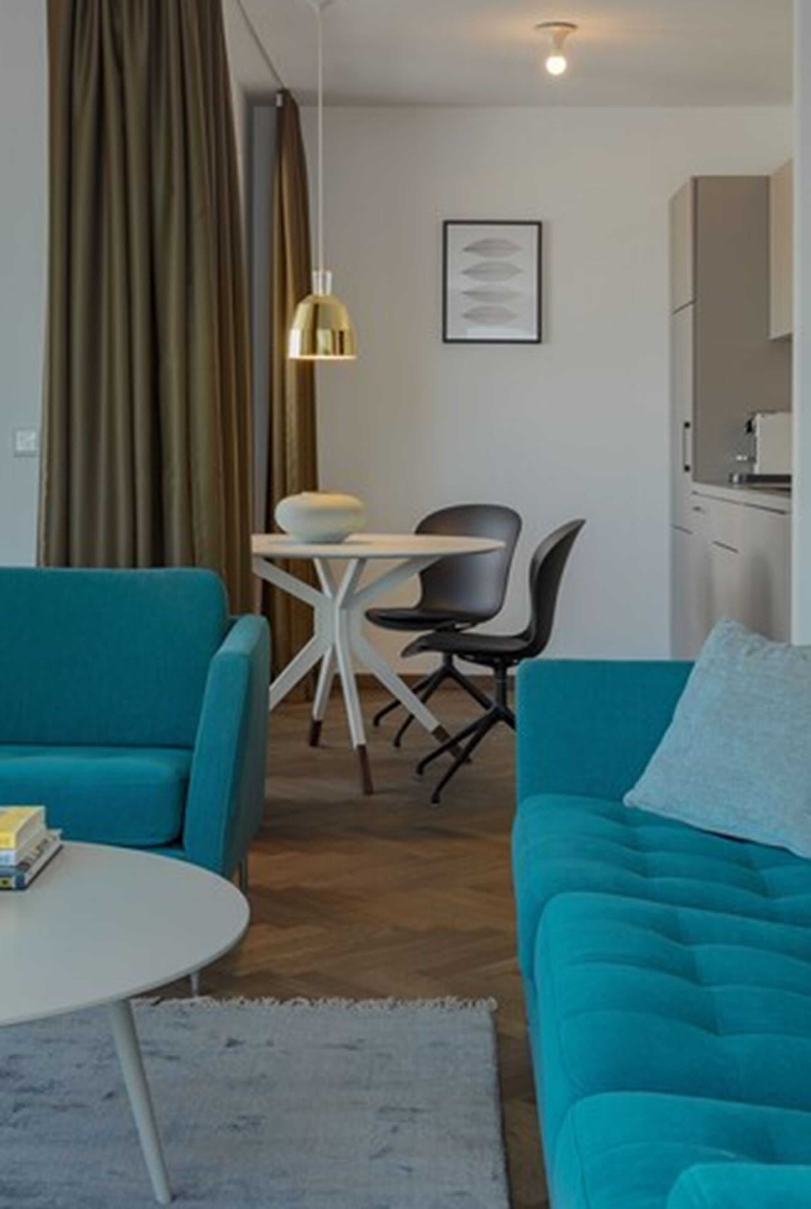 Una sala de estar moderna con sofás color turquesa, una mesa de centro redonda y un comedor con mesa blanca y sillas negras.