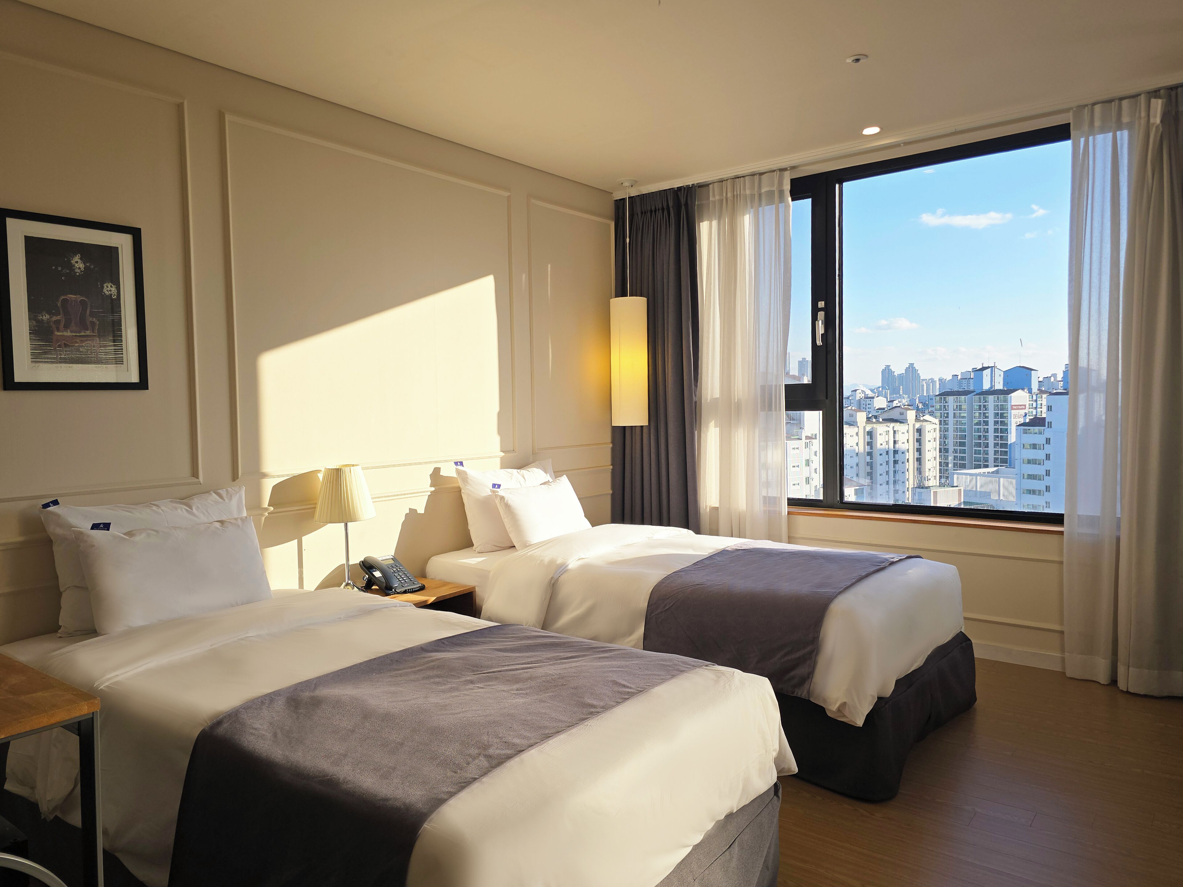 A hotel room with two beds, a city view, and a framed picture on the wall.