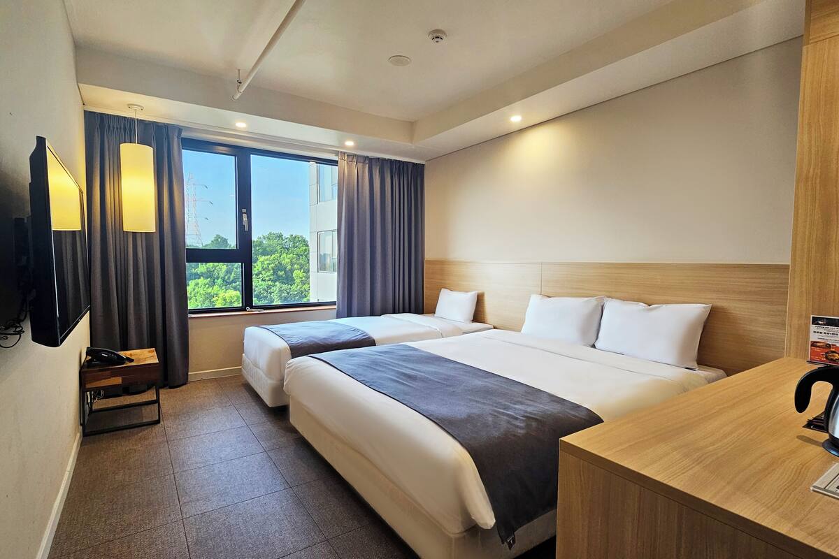 A hotel room with two beds, a desk, a telephone, and a window with curtains.