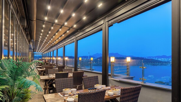 A restaurant with tables and chairs, large windows, and a view of a body of water and mountains. - JK Blossom Hotel (Seoul)