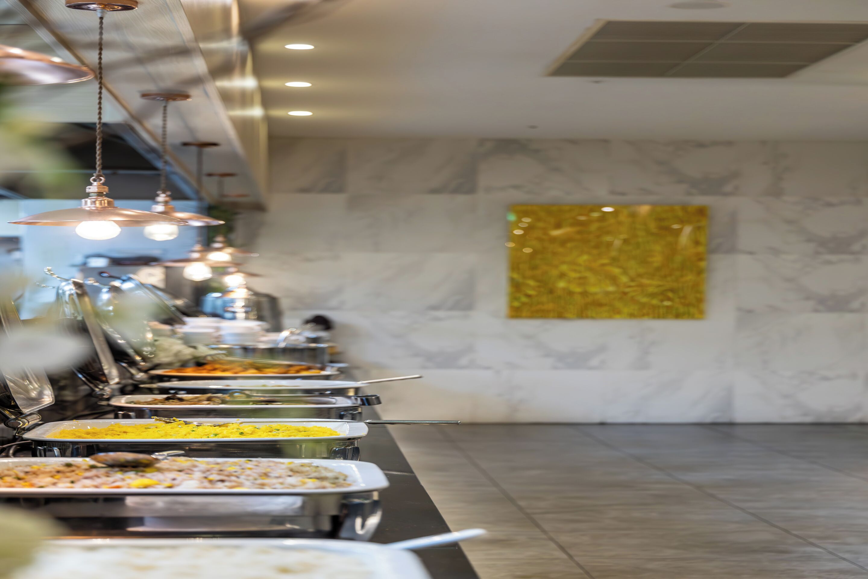 Zona de bufé con varias estaciones de comida y lámparas colgantes.