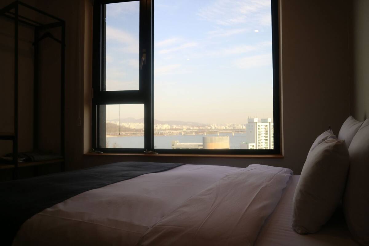 A bedroom with a large window, a bed, and a view of a cityscape.