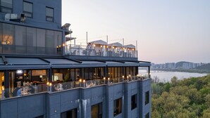 A modern building with a rooftop terrace featuring outdoor seating and a view of a river. - JK Blossom Hotel (Seoul)