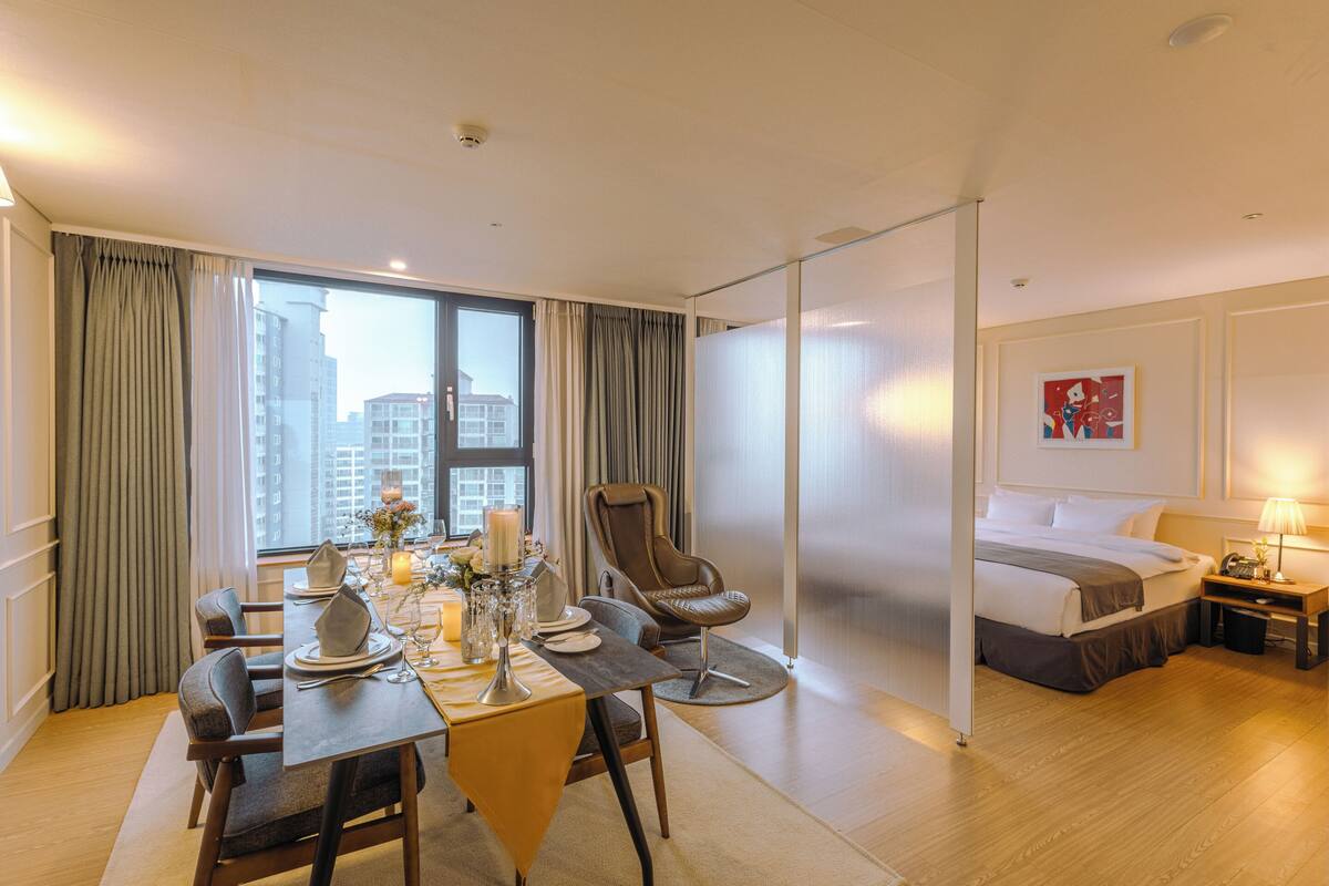 A hotel room with a dining area, a bed, and a view of the cityscape.