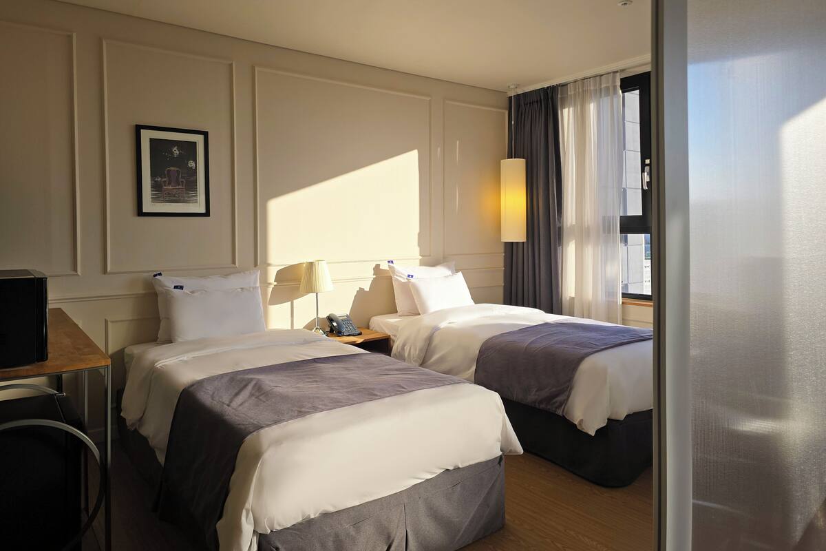 A hotel room with two beds, a desk, a chair, a phone, and a window with curtains.