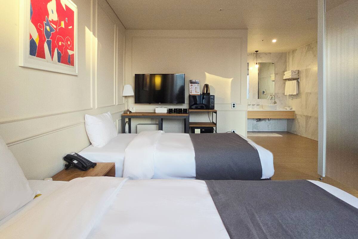 A hotel room with two beds, a desk with a TV, a coffee maker, and a bathroom with a sink and mirror.