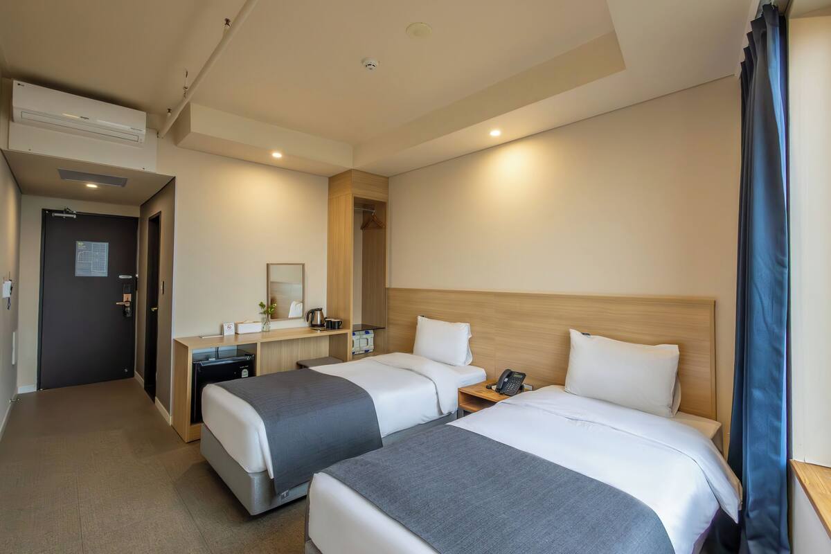 A hotel room with two beds, a desk with a telephone, a mirror, and a wardrobe.
