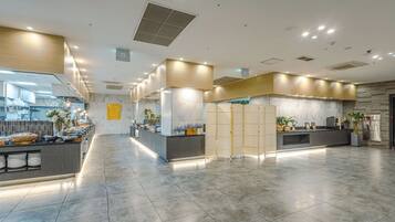 A spacious lobby with a reception desk, seating area, and a kitchen in the background.