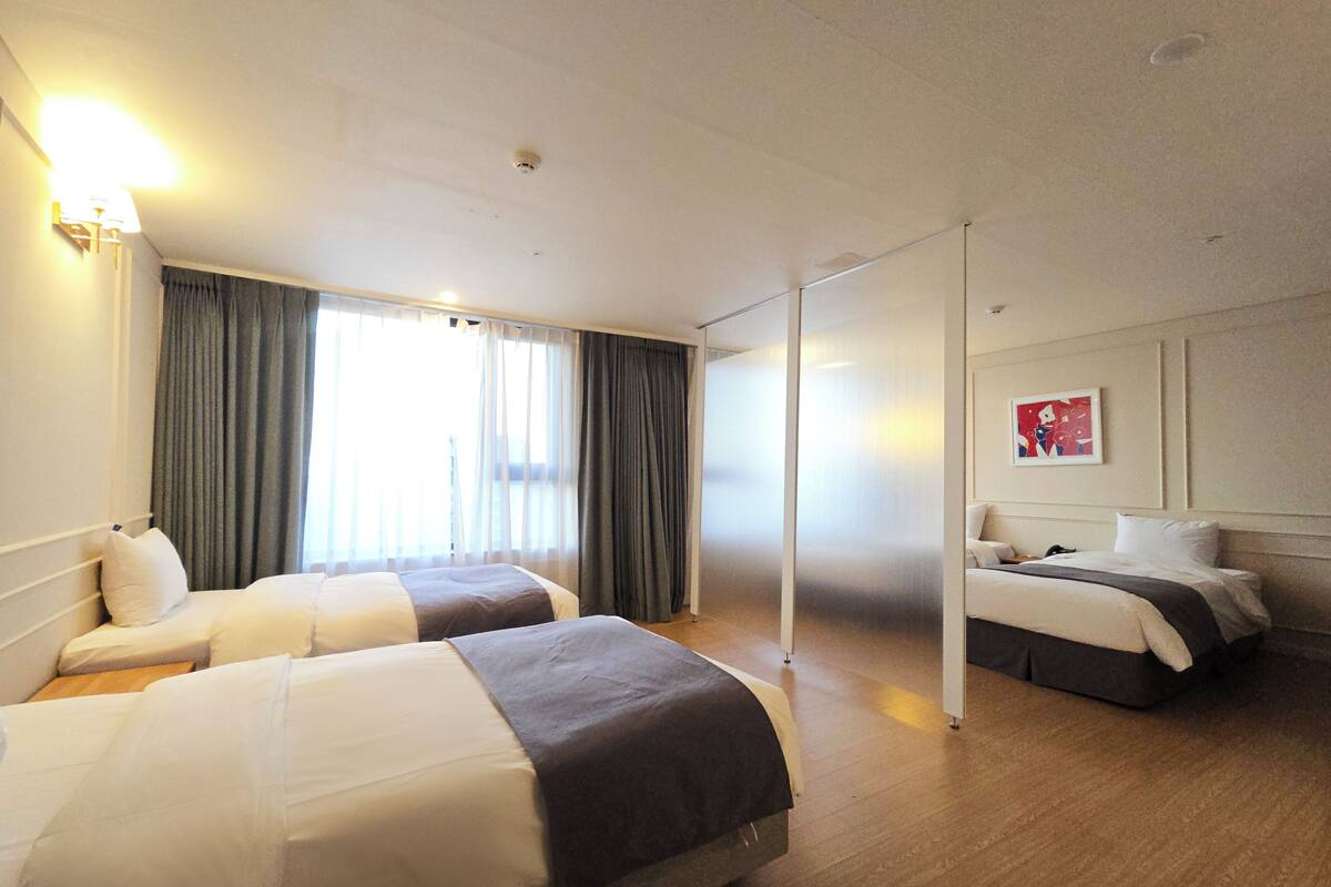 A hotel room with two beds, a large window with curtains, a flat-screen TV, and a painting on the wall.