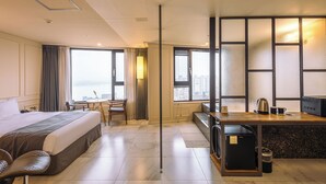 A hotel room with a bed, desk, kitchenette, and large windows offering a city view. - JK Blossom Hotel (Seoul)
