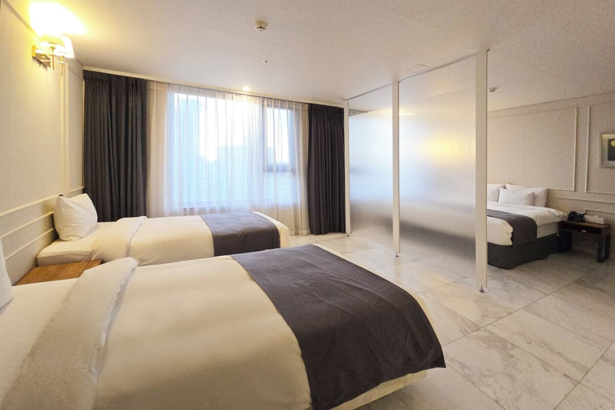A hotel room with two beds, a large window with curtains, a flat-screen TV, and a bedside table.