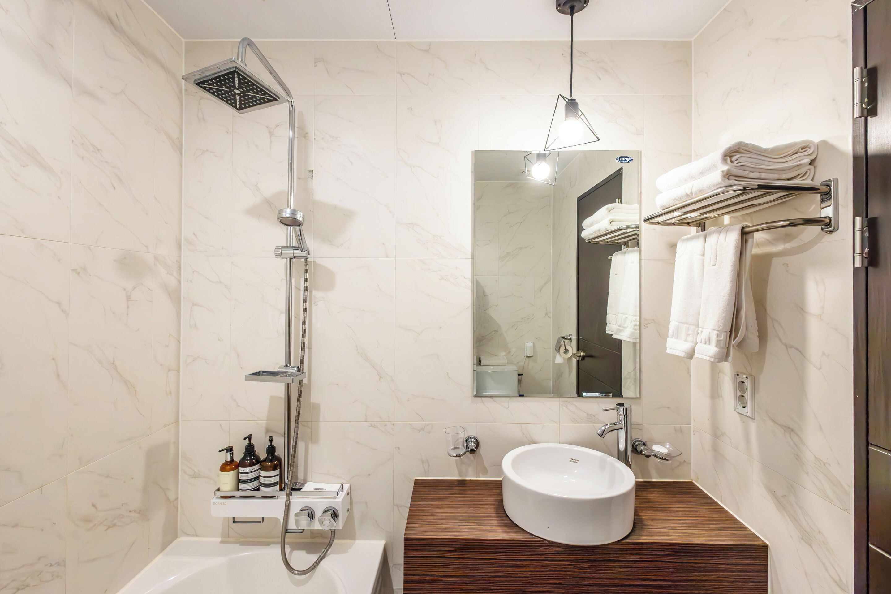 Un baño moderno con una bañera independiente, un lavabo integrado con tocador de madera, un perchero de pared y un espejo grande.