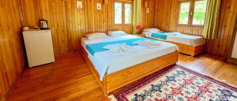 A wooden cabin with two beds, a small kitchenette, and a window with curtains.
