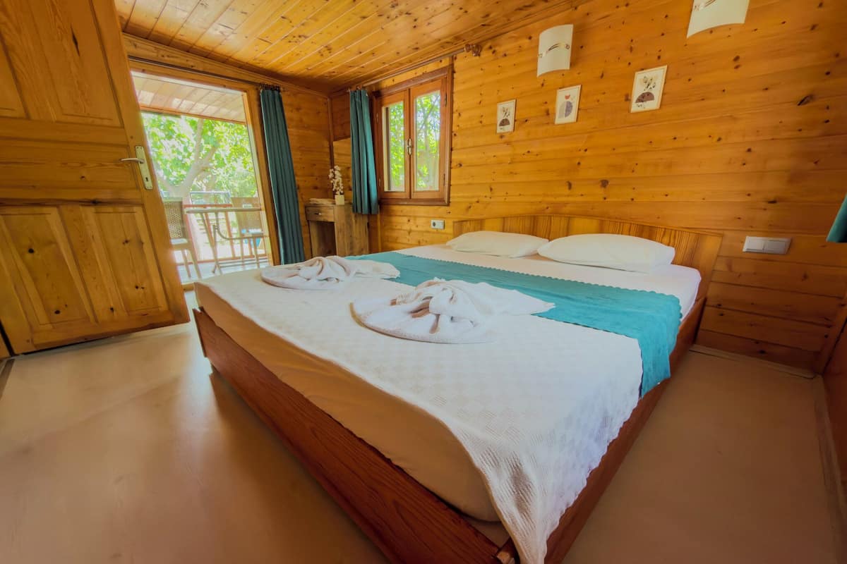 A wooden cabin bedroom with a bed, curtains, and a window.