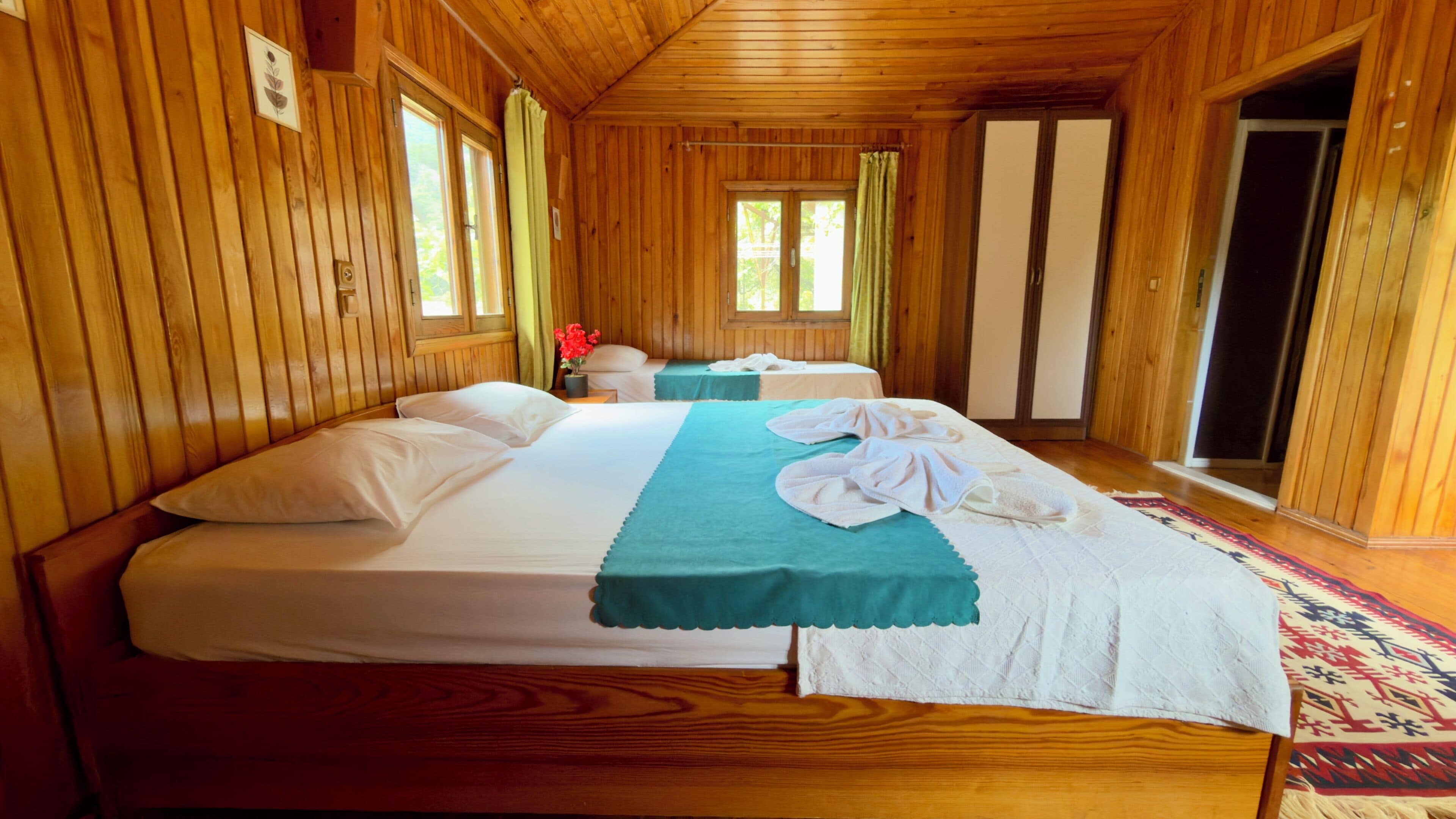 Habitación de cabaña de madera con una cama grande, otra más pequeña y una ventana con cortinas.