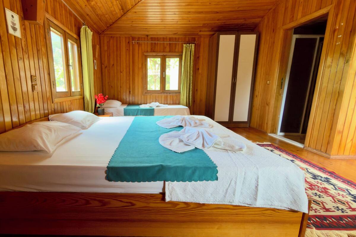 A wooden cabin room with a large bed, a smaller bed, and a window with curtains.