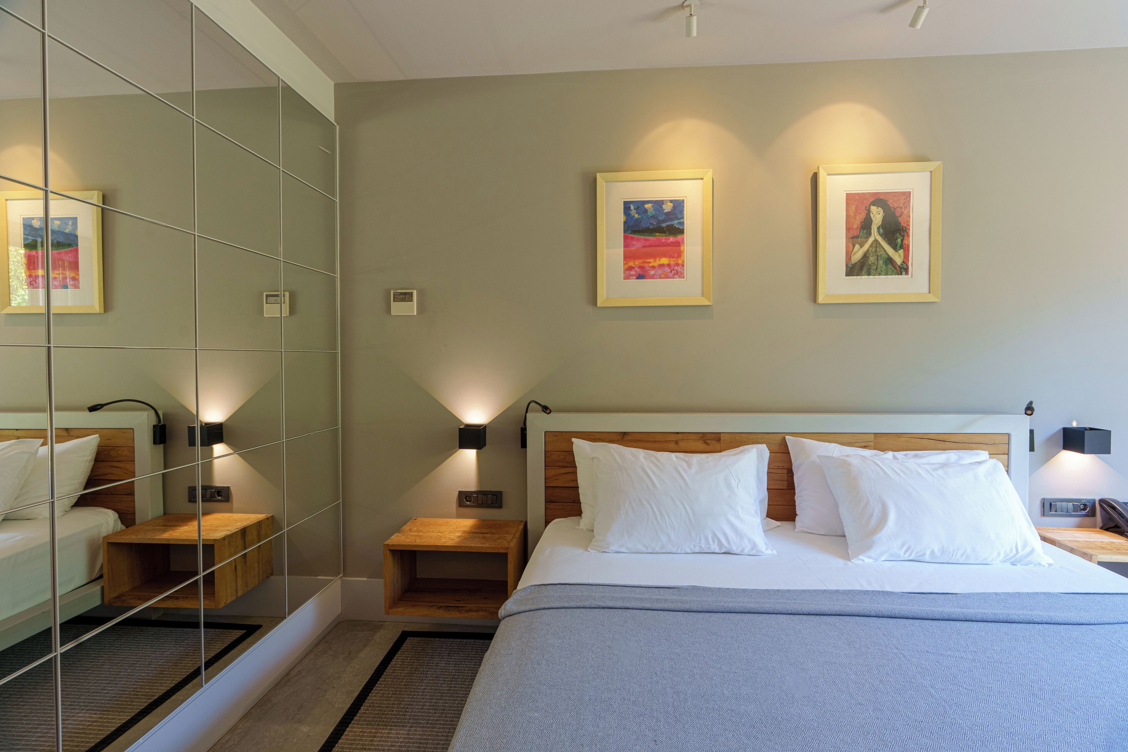 Ein Hotelzimmer mit Bett, Nachttischen, einem Spiegel und Kunstwerken an den Wänden.