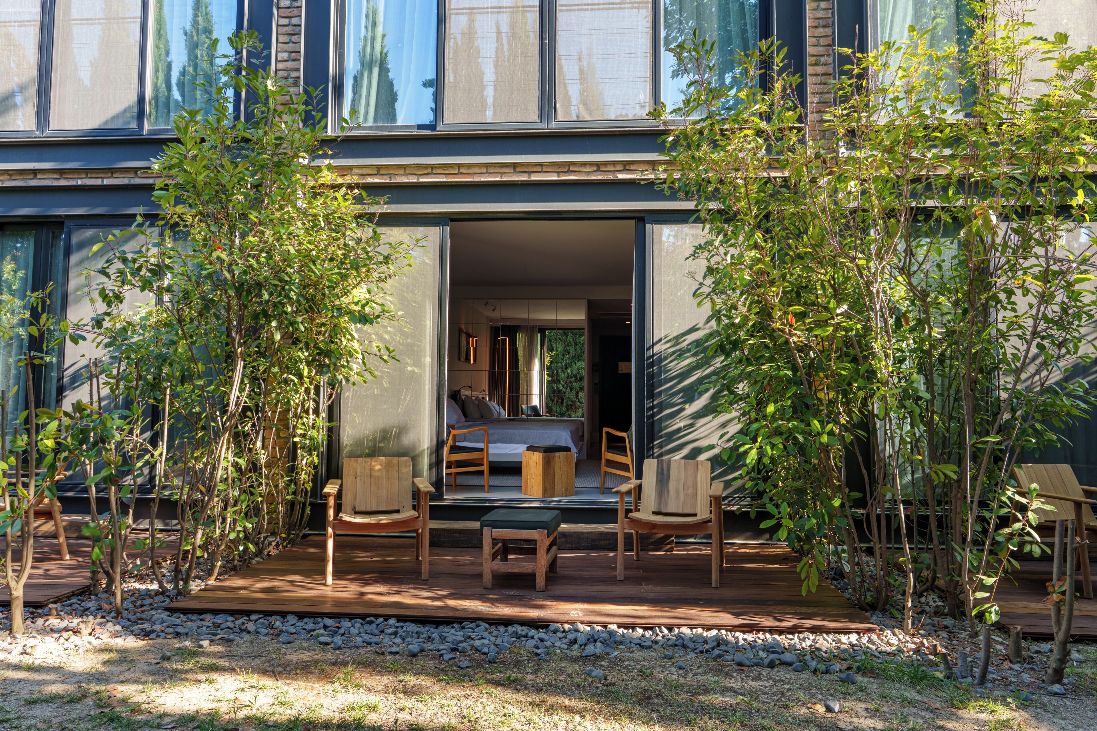 A modern building with a large glass door leading to a bedroom with a bed, two chairs, and a small table.